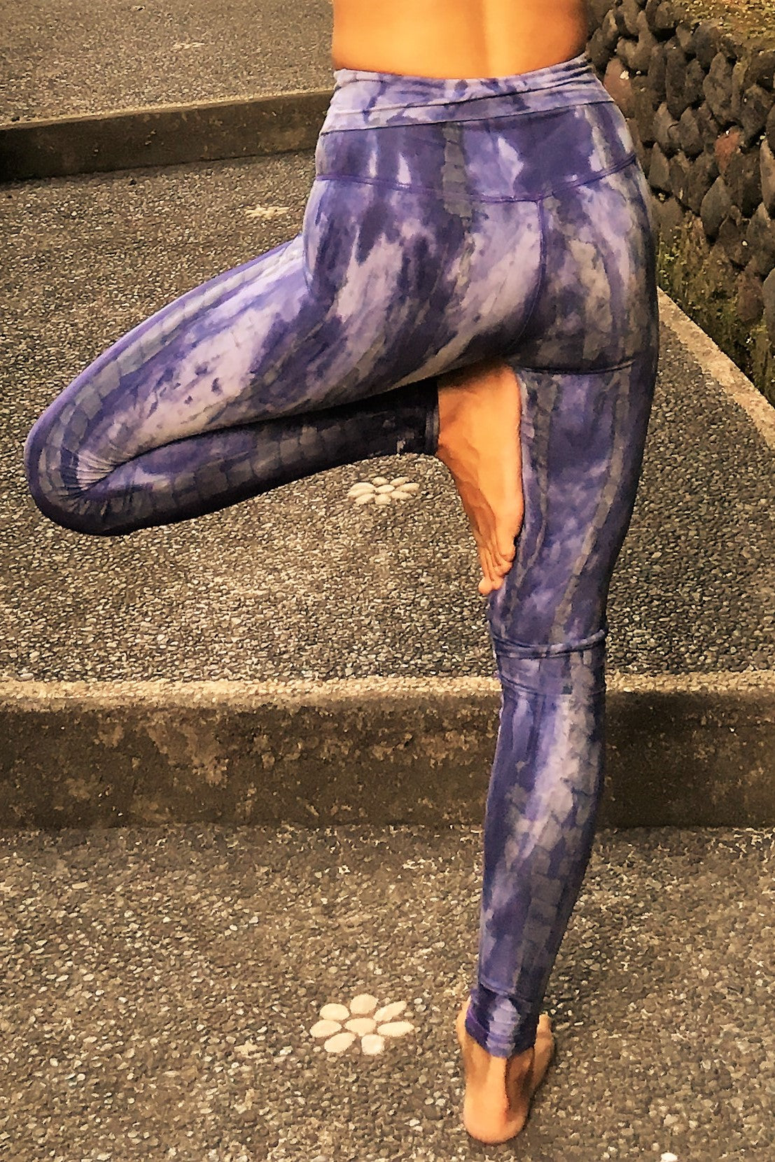 Woman in tree pose wearing fold over waist yoga pants in cool purple hues with grey and white highlights.