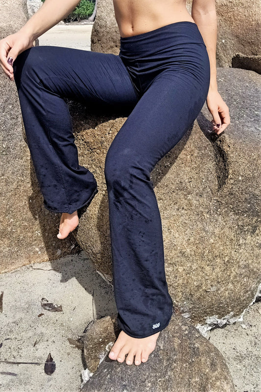 Side view of Onyx Flared Bottom Yoga Pants by Lotus Tribe Clothing with small white lotus flower embroidery on bottom of left leg.