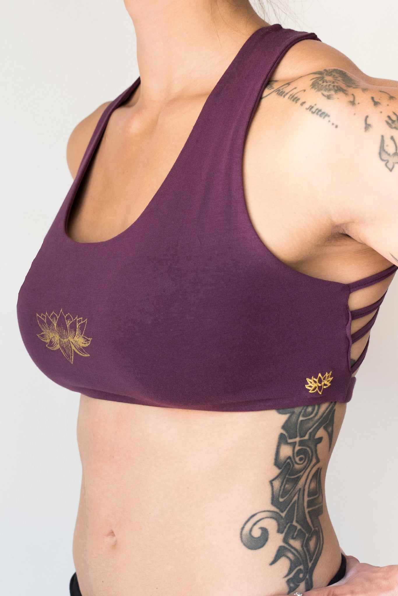 Plum sports bra with gold lotus flower design on front that has 4 criss cross straps in back and has enough support for down dog and other yoga poses.