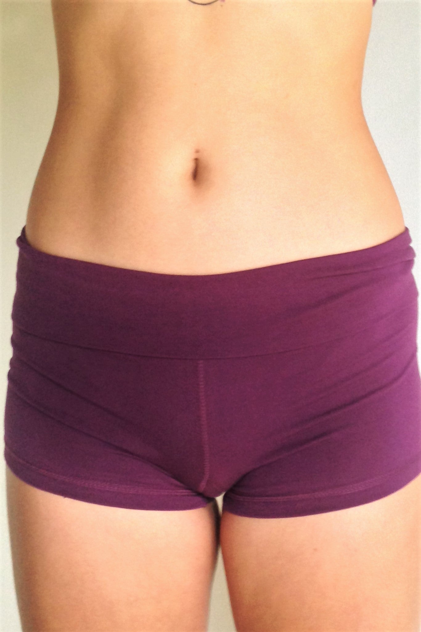 Front view of solid Plum purple yoga shorts with fold over waist, can be worn higher waisted, or low on the hips. Small black Lotus Flower embroidery. 90% cotton 10% spandex.