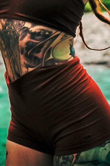 High waisted yoga shorts in solid Rust color with small black lotus flower embroidery on bottom of left leg.