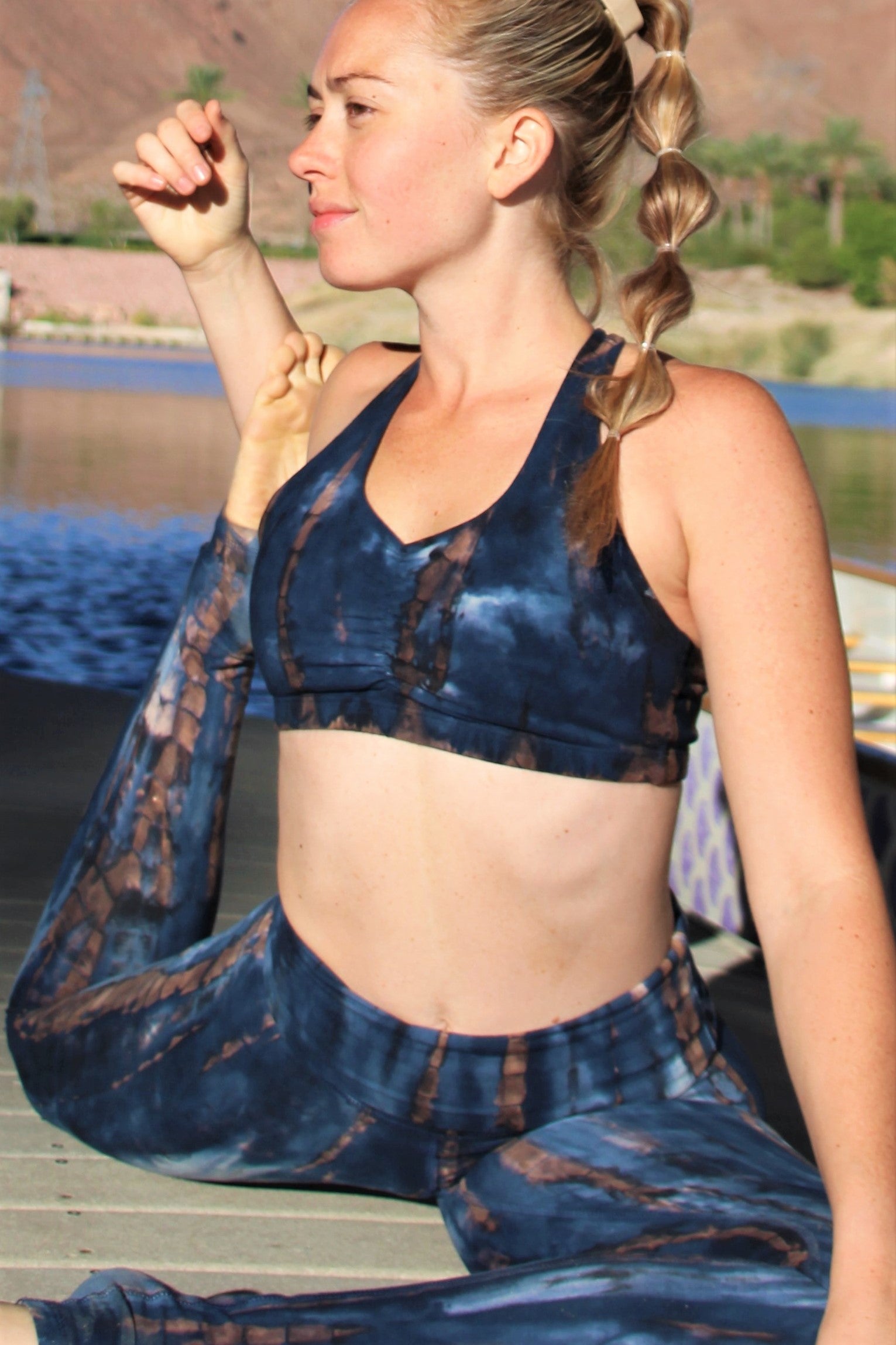 Gorgeous blue tie dyed sportsbra with brown streaks and white highlights. Very earthy colors made from 90% organic cotton with 10% spandex. Shown on model with matching pants in yoga pose outdoors in nature.