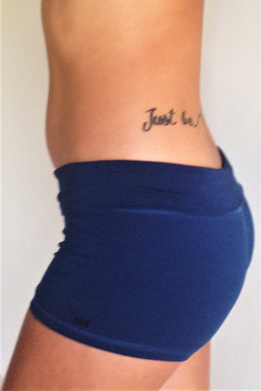 Side view of solid Cobalt blue yoga shorts with fold over waist, can be worn higher waisted, or low on the hips. Small black Lotus Flower embroidery. 90% cotton 10% spandex.