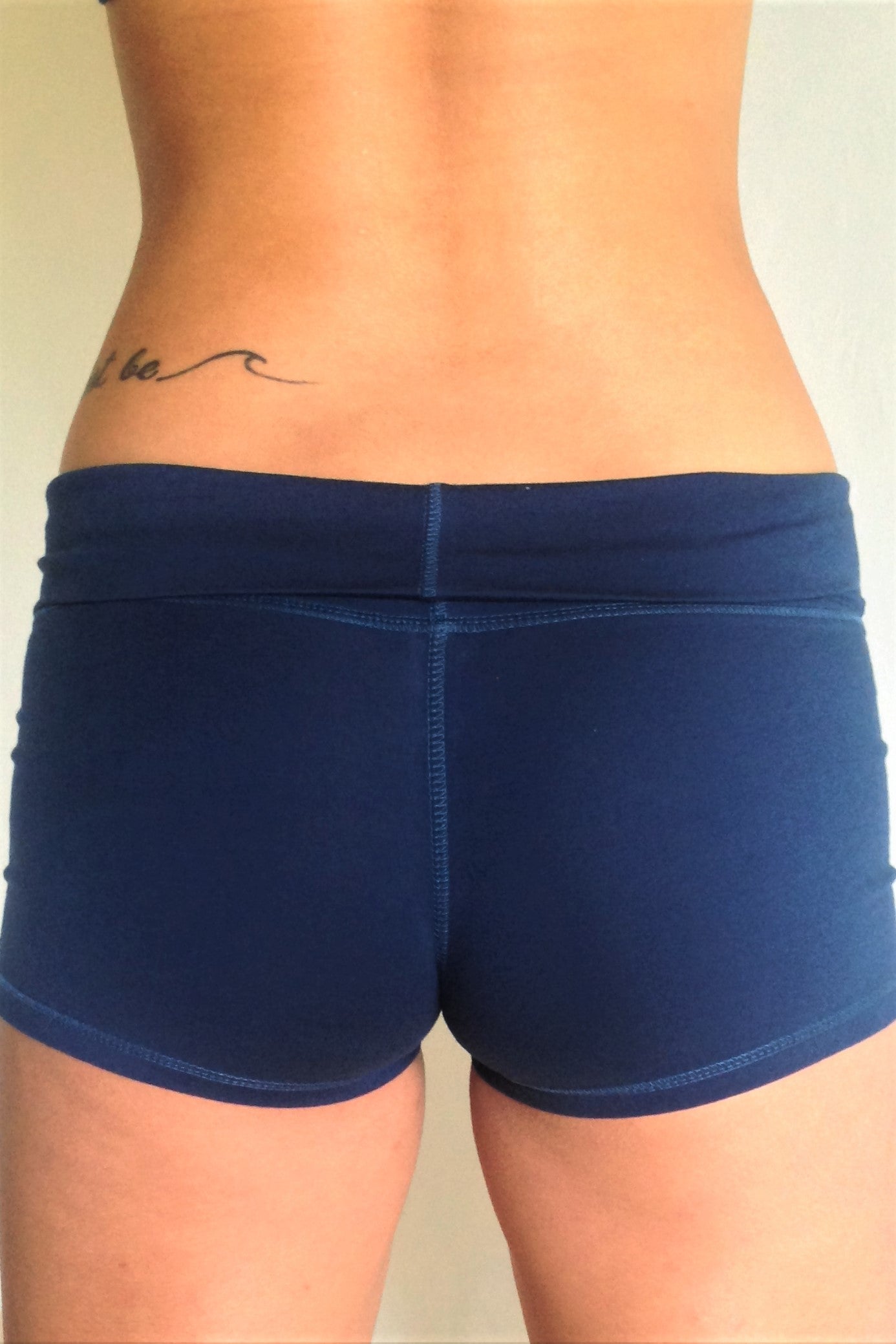 Back view of solid Cobalt blue yoga shorts with fold over waist, can be worn higher waisted, or low on the hips. Small black Lotus Flower embroidery. 90% cotton 10% spandex.