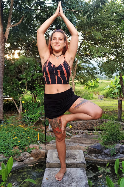 Woman is tree pose wearing Fire tie dye Blissed Out Crop Top with Onyx Cinch Skirt. 