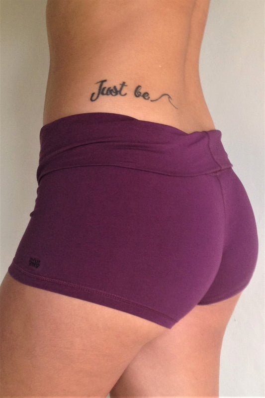 Side view of solid Plum purple yoga shorts with fold over waist, can be worn higher waisted, or low on the hips. Small black Lotus Flower embroidery. 90% cotton 10% spandex.