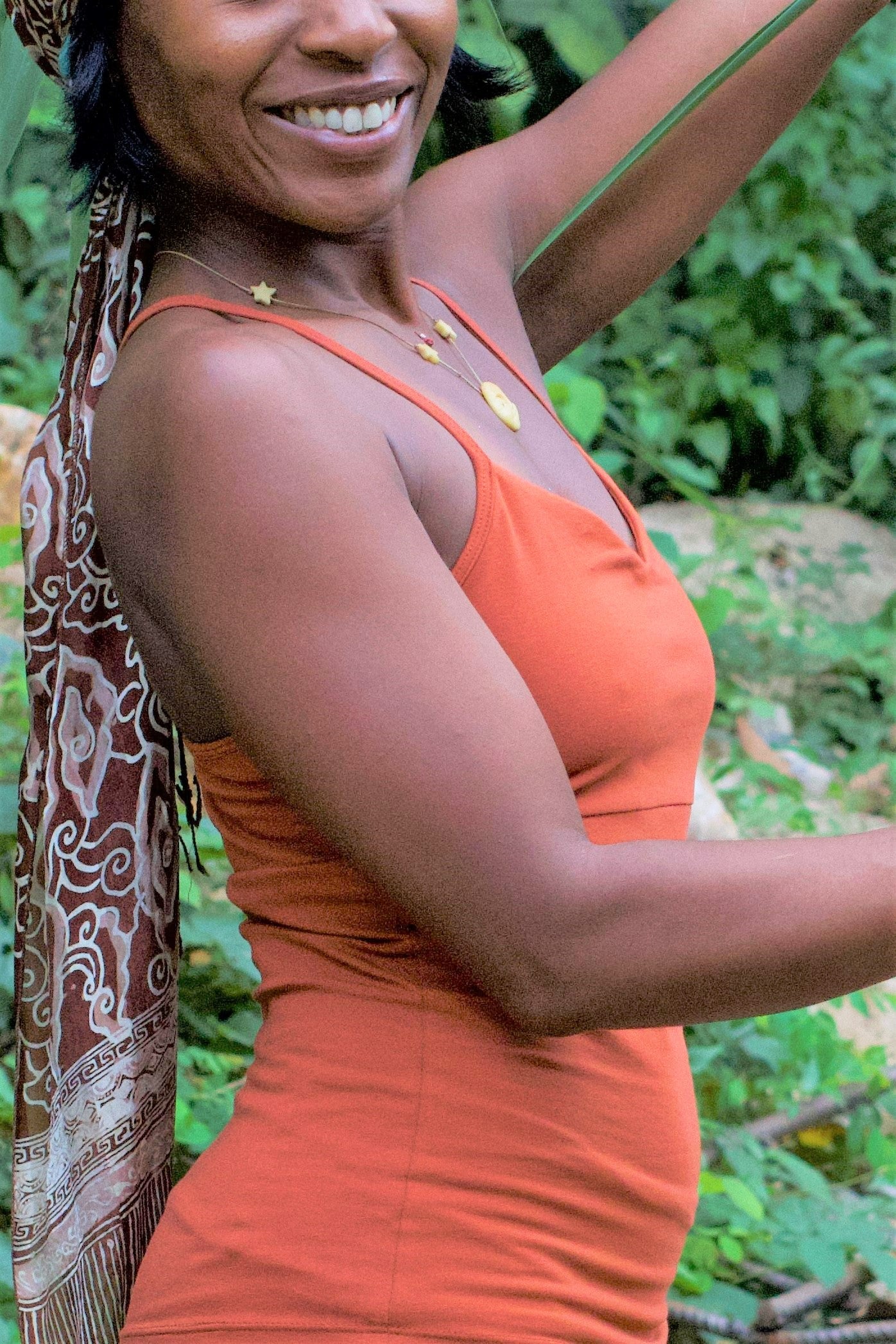 Side view of Rust Anand Tank wtih thin spaghetti straps, gold jewelry and beautiful smile.